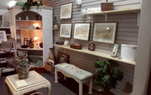 Interior of thrift shop. Tables, pictures, on wall, and a curio cabinet in view.
