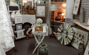 Interior of thrift shop. Tables, pictures, on wall, and a curio cabinet in view.